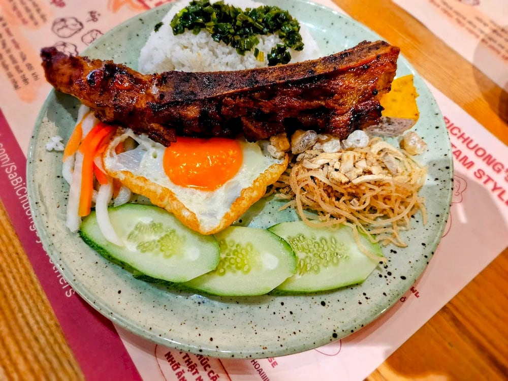 The combo of grilled pork chop and rib, topped with full sides, is a top pick for those wanting the complete broken rice experience